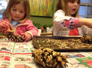 The girls cover pinecones they collected on a walk in honey and roll them in bird-seed.